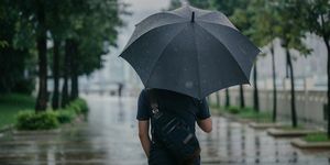 поглед отпозади на паметног узрочног мушкарца који држи кишобран и шета парком у кишном урбаном граду
