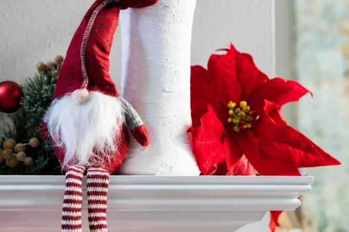 класична норвешка празнична декорација божићног гнома који седи на белом модерном плашту са белом вазом са еукалиптусом и цветом божићне звезде