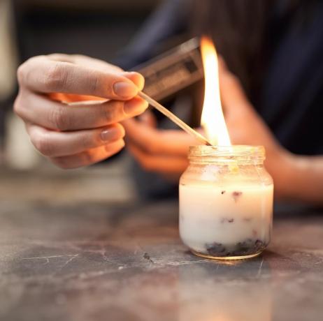 обрезивање анонимне жене са запаљеном шибицом пали ароматичну свећу у стакленој посуди постављеној на мермерни сто код куће