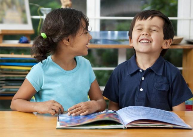 двоје деце која се смеју уживају у књизи у школи