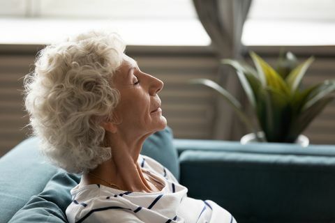 поглед са стране лице шездесетих година зрела мирна жена затворене очи уживајте на свежем ваздуху проводите време код куће наслоњени на софу, одмарајући се добијајући менталну и физичку снагу свесност медитација за старије особе концепт