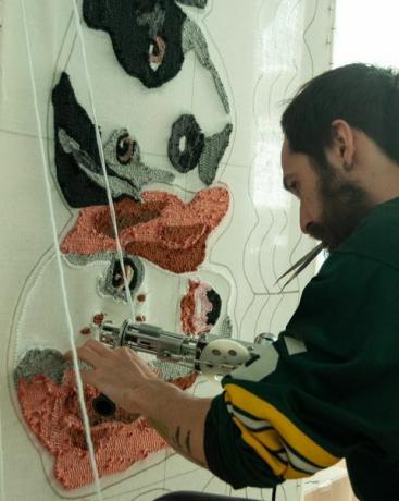 30-годишњи шпански латино брадати мушкарац у рагби дресу, у својој радионици ради на ручно рађеним ћилимима направљеним од тафтинг пиштоља и акрилних влакана, са дизајном тепиха за псе