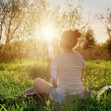 млада жена која седи у јога положају и ужива у заласку сунца у природи